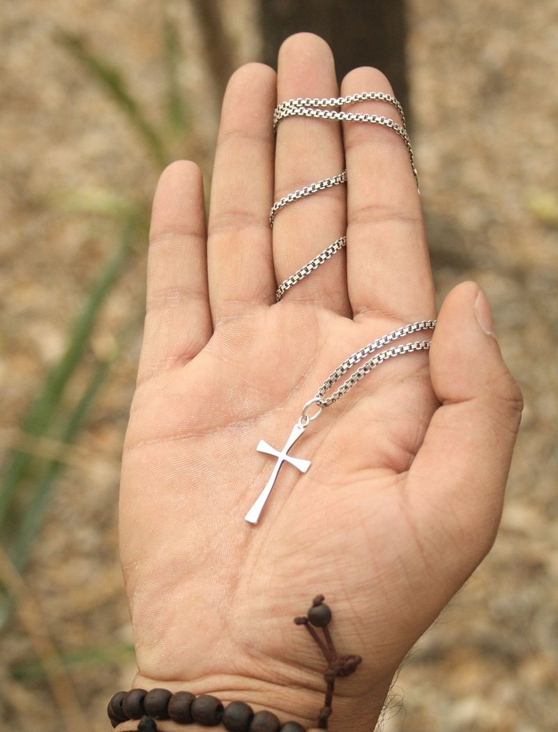 Kaulakoru, jossa risti, on kiedottu sormien ympärille. Risti on keskellä kämmentä.